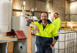 Kurrajong Timber senior supervisor Craig Lees standing among machinery, with employees working behind him.