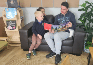 Chris Heaslip sitting on a couch reading a book to two children.