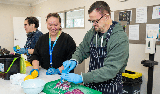 Kurrajong staff member helping Kurrajong client to cut onions